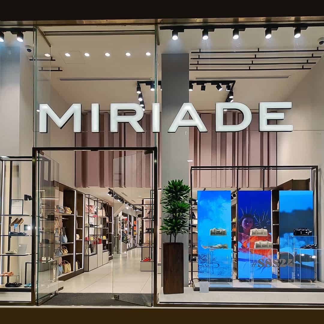 Vetrina di negozio di moda con display digitale e scaffali di accessori, ambiente elegante e moderno.