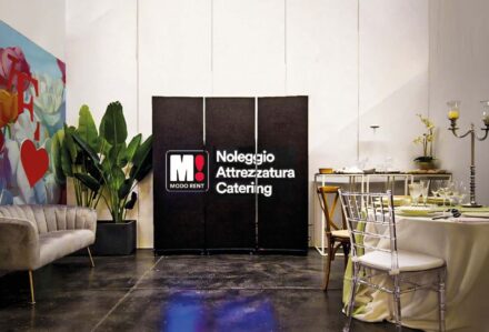 Spazio per eventi con tavolo elegante, decorazioni e piante verdi, ideale per catering e noleggio attrezzature.