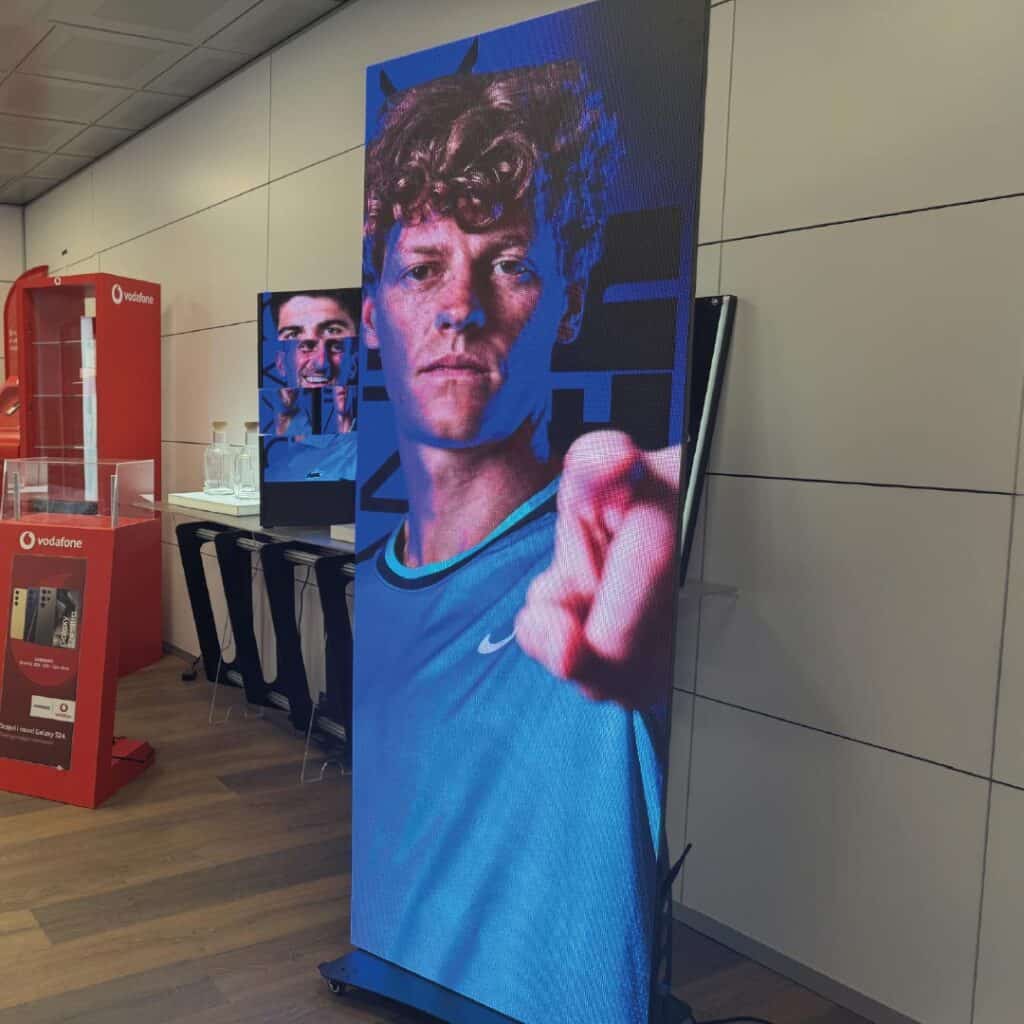 Display digitale pubblicitaria in un negozio Vodafone con immagine di un giovane uomo che punta verso la fotocamera.