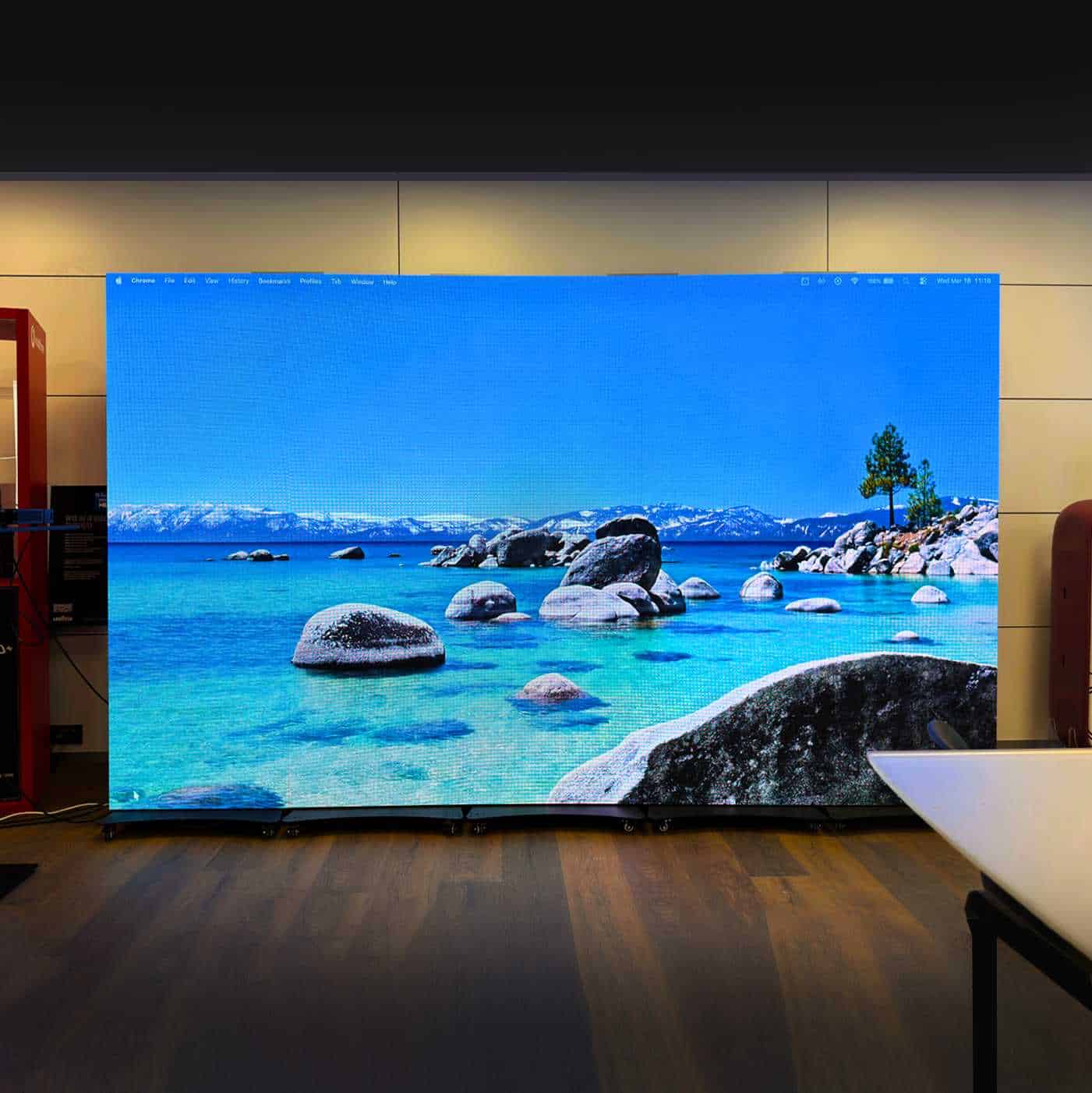 Televisore LED di grandi dimensioni con immagine di un paesaggio marino e montagne sullo sfondo, ideale per ambienti moderni e tecnologici.