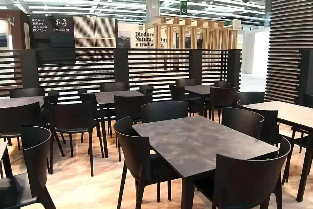 Un ambiente da bar moderno, con numerosi arredi forniti da Modorent. Sono visibili tavoli e sedie neri, circondato da pareti divisorie in legno. La segnaletica del marchio di vendita al dettaglio è visibile sopra le pareti divisorie.