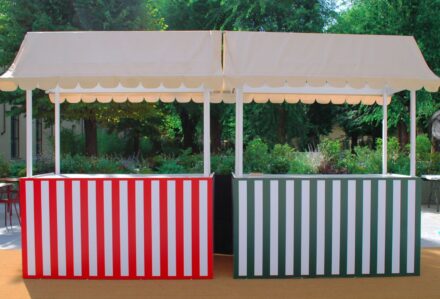 Stand gastronomico con tende bianche e pannelli a righe rosse e verdi, ideale per eventi all'aperto e fiere, con un ambiente naturale sullo sfondo.