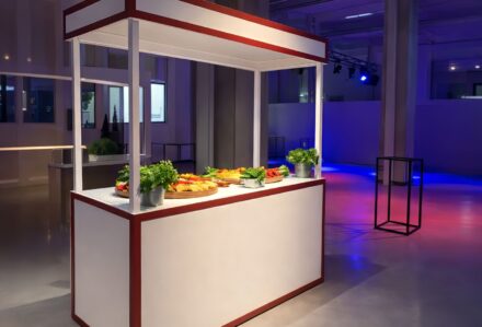 Banco buffet con piatti vari e decorazioni verdi in un ambiente moderno e ben illuminato.