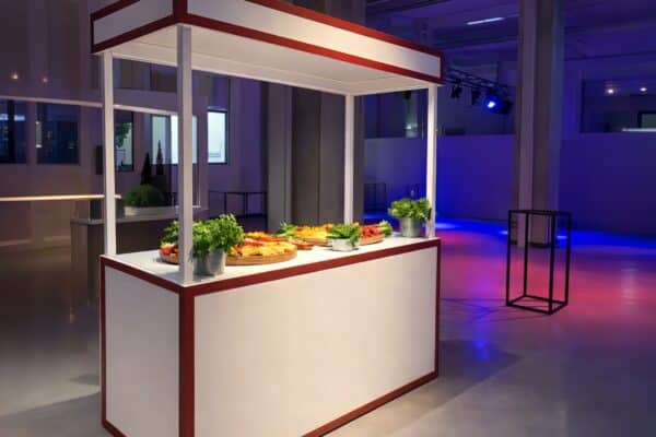 Banco buffet con piatti vari e decorazioni verdi in un ambiente moderno e ben illuminato.
