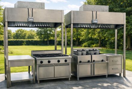 Cucina professionale all'aperto in acciaio inox con barbecue e piani di lavoro in un giardino verde.