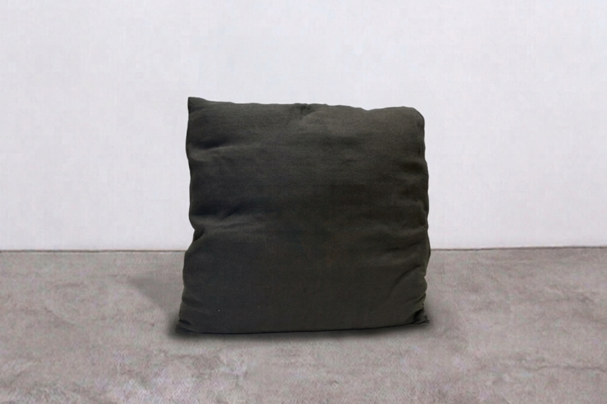 Cuscino nero in tessuto morbido su pavimento in cemento, ideale per arredi moderni e minimalisti, perfetto come elemento decorativo o di comfort in ambienti interni.