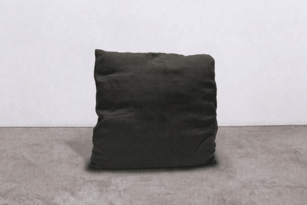 Cuscino nero in tessuto morbido su pavimento in cemento, ideale per arredi moderni e minimalisti, perfetto come elemento decorativo o di comfort in ambienti interni.
