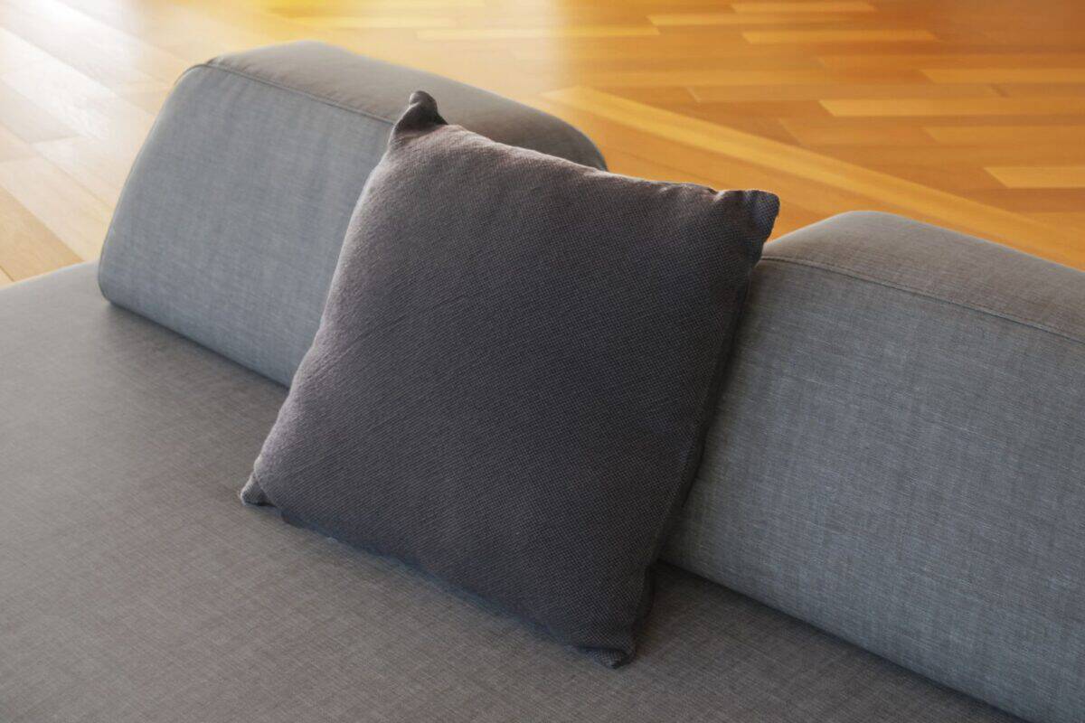 Cuscino grigio scuro su divano moderno in soggiorno con pavimento in legno chiaro.