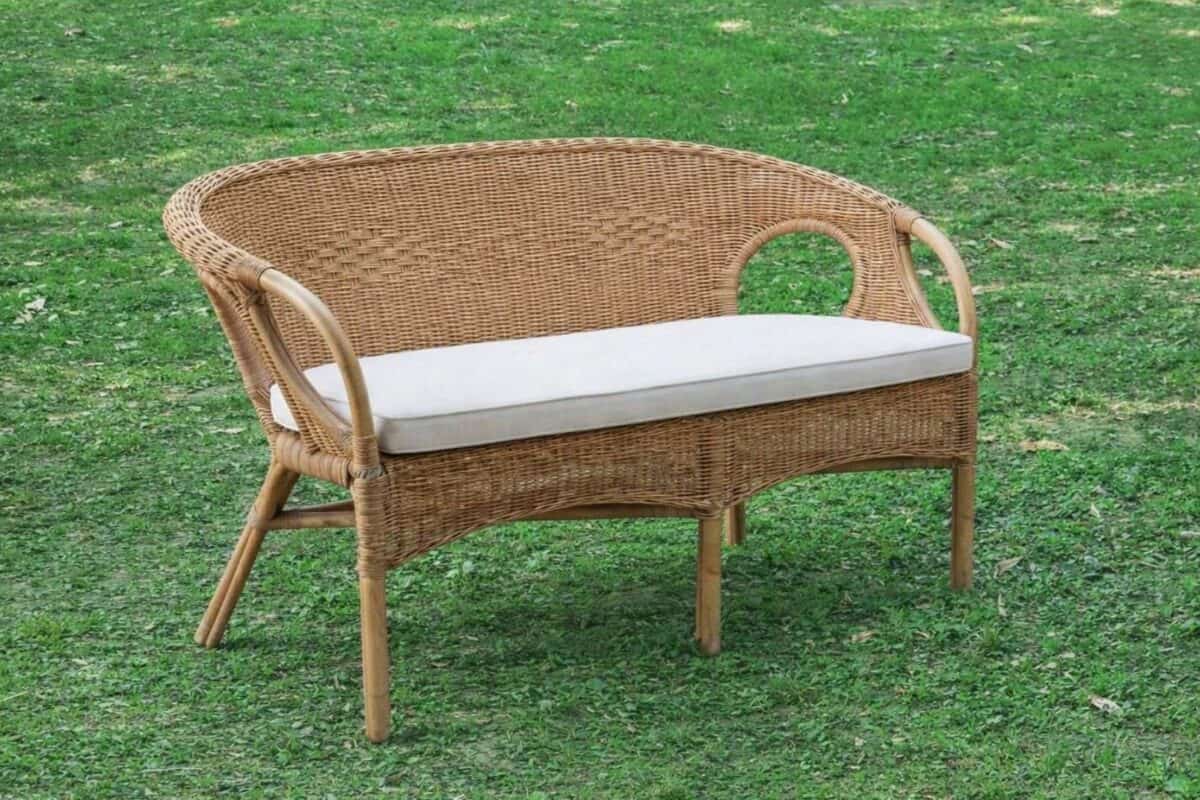Divano in rattan con cuscino bianco su prato verde, perfetto per esterni e giardini.