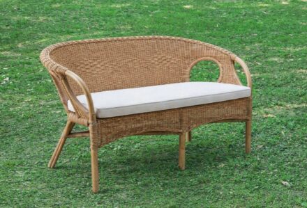 Divano in rattan con cuscino bianco su prato verde, perfetto per esterni e giardini.
