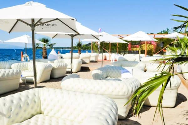 Divano gonfiabile grande bianco posizionato sulla spiaggia con ombrelloni e vista mare, ideale per relax e comfort all'aperto.