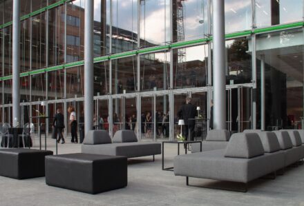 Elegante divano lounge angolare in tessuto grigio scuro, ideale per ambienti moderni e professionali, perfetto per aree di attesa o spazi relax all'aperto o al chiuso.
