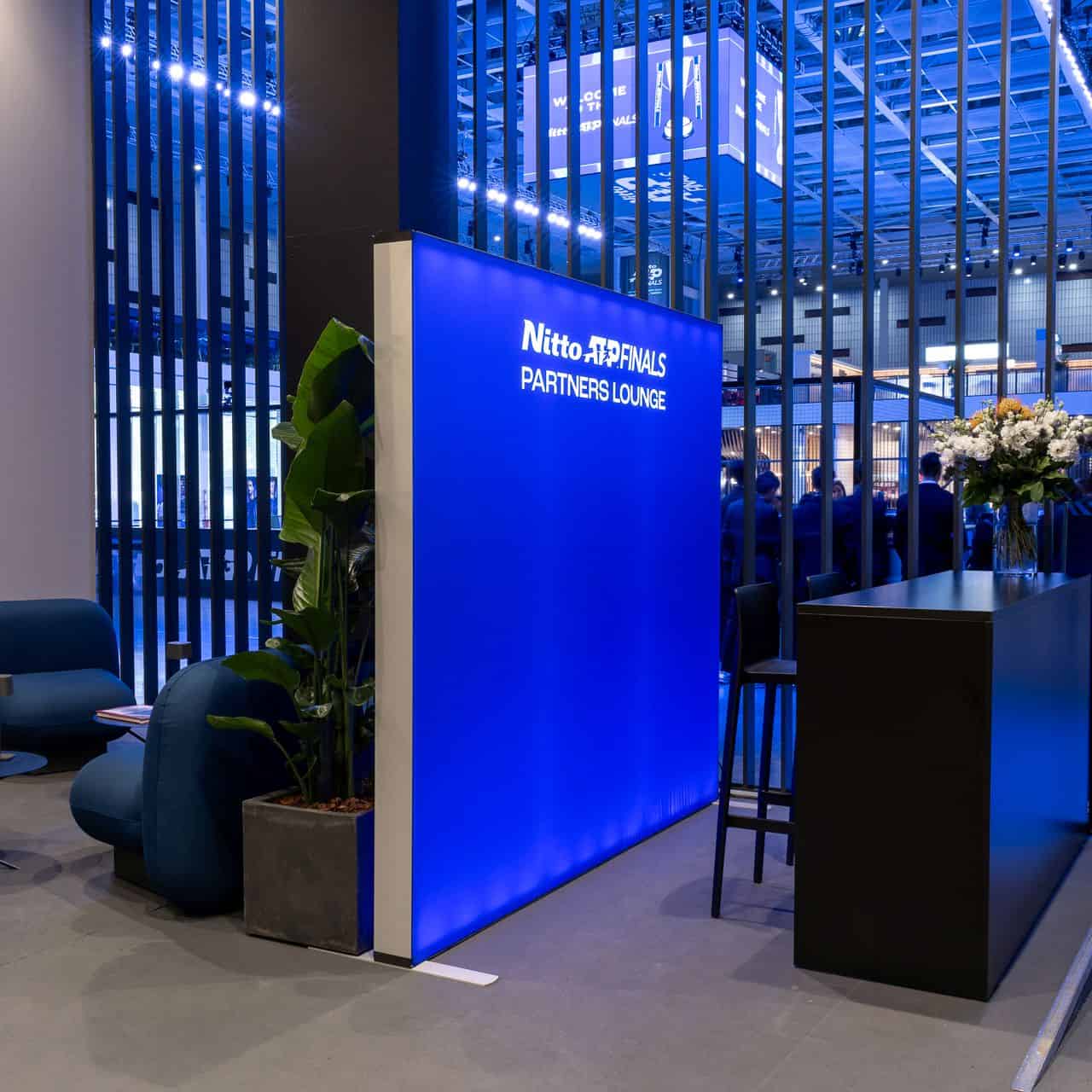 Area lounge Nitto ATP Finals con pannello luminoso blu e arredi moderni, atmosfera elegante e accogliente.