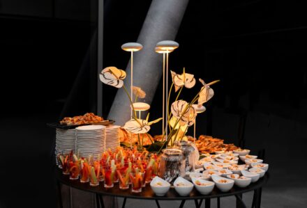 Spuntino di antipasti e finger food con presentazione elegante su tavolo nero, con decorazioni di fiori e luci soffuse, ideale per eventi e feste sofisticate.