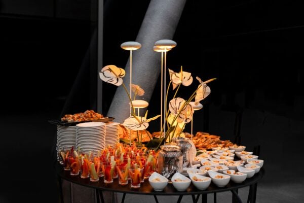Lampada da tavolo modello Nuvola bianca alta 65 cm accesa all'interno di una composizione floreale, disponibile a noleggio con Modorent per eventi e buffet.