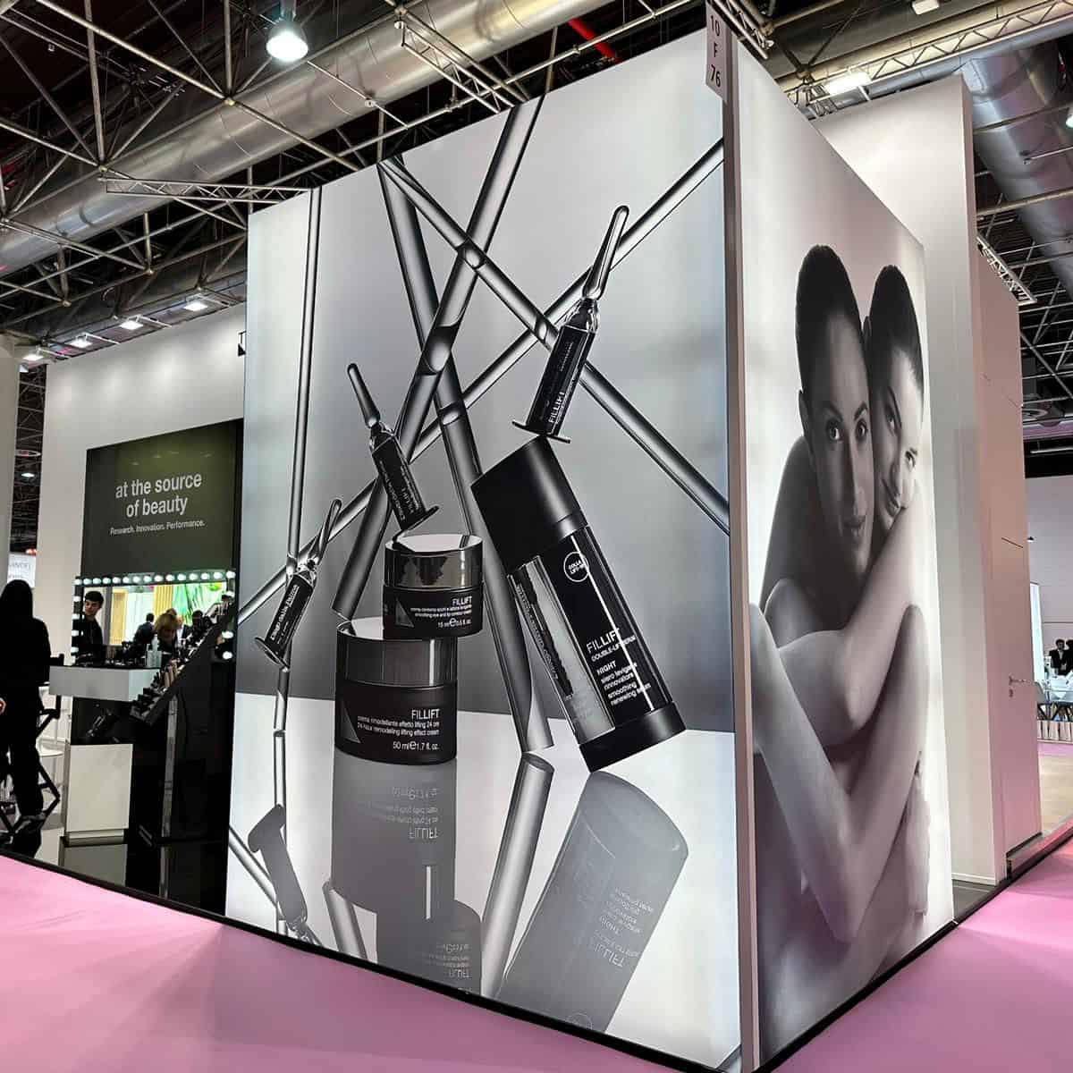 Stand espositivo di prodotti di bellezza con sieri e creme, decorato con immagini di due donne sorridenti, in un evento fieristico.