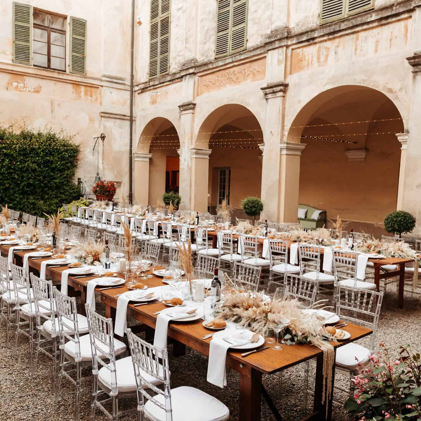 Elegante tavola all'aperto in un cortile storico con decorazioni floreali e luci soffuse, ideale per eventi e ricevimenti.