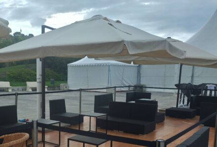 Area lounge all'aperto con sedie e ombrelloni, ideale per eventi e relax, con sfondo di tende bianche e paesaggio naturale.