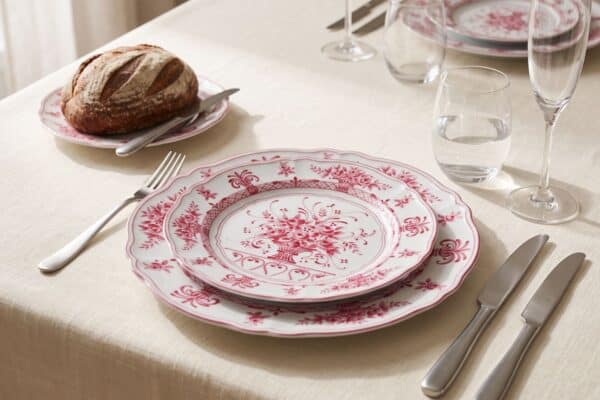 Piatti in porcellana con motivo floreale rosso su tavola elegante per cena.