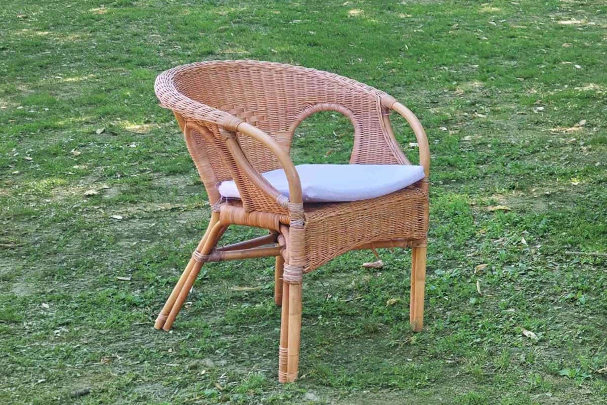 Sedia in vimini con cuscino bianco su prato verde, ideale per arredamento esterno e giardini.