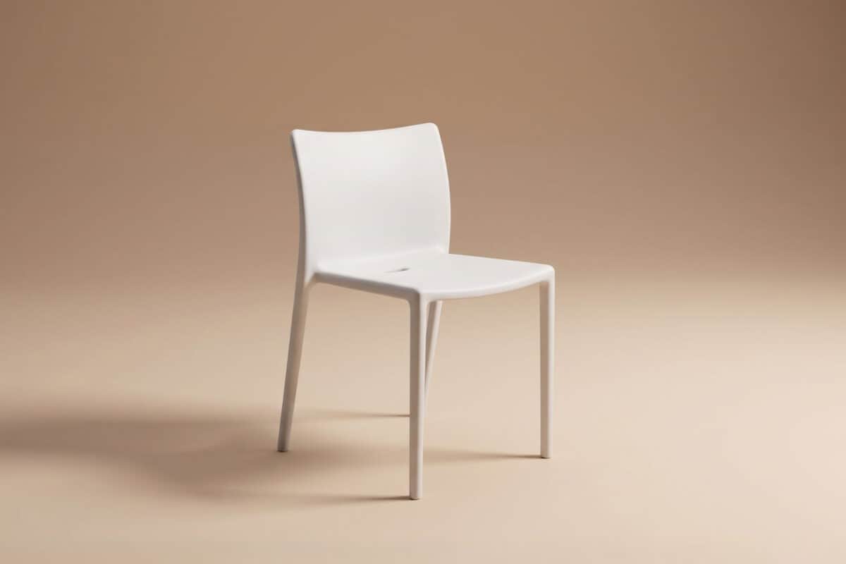 Sedia moderna bianca con schienale curvo e gambe sottili su sfondo beige neutro.