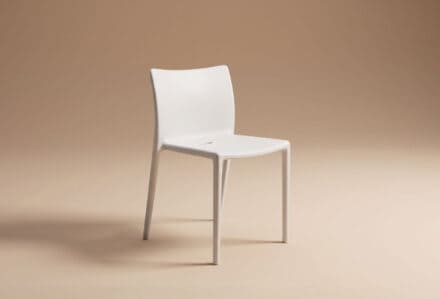 Sedia moderna bianca con schienale curvo e gambe sottili su sfondo beige neutro.
