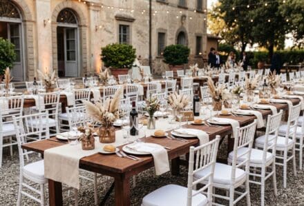 Tavolo per evento all'aperto con sedie bianche e decorazioni floreali in un cortile storico.