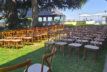 Sedie in legno disposte all'aperto in un giardino con alberi e gazebo, ideale per eventi e cerimonie all'aperto.