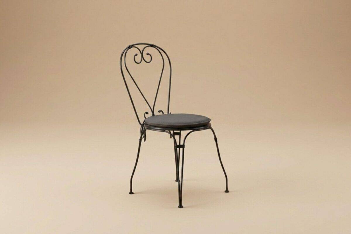 Sedia in ferro battuto con schienale decorato a cuore, stile vintage, su sfondo neutro.