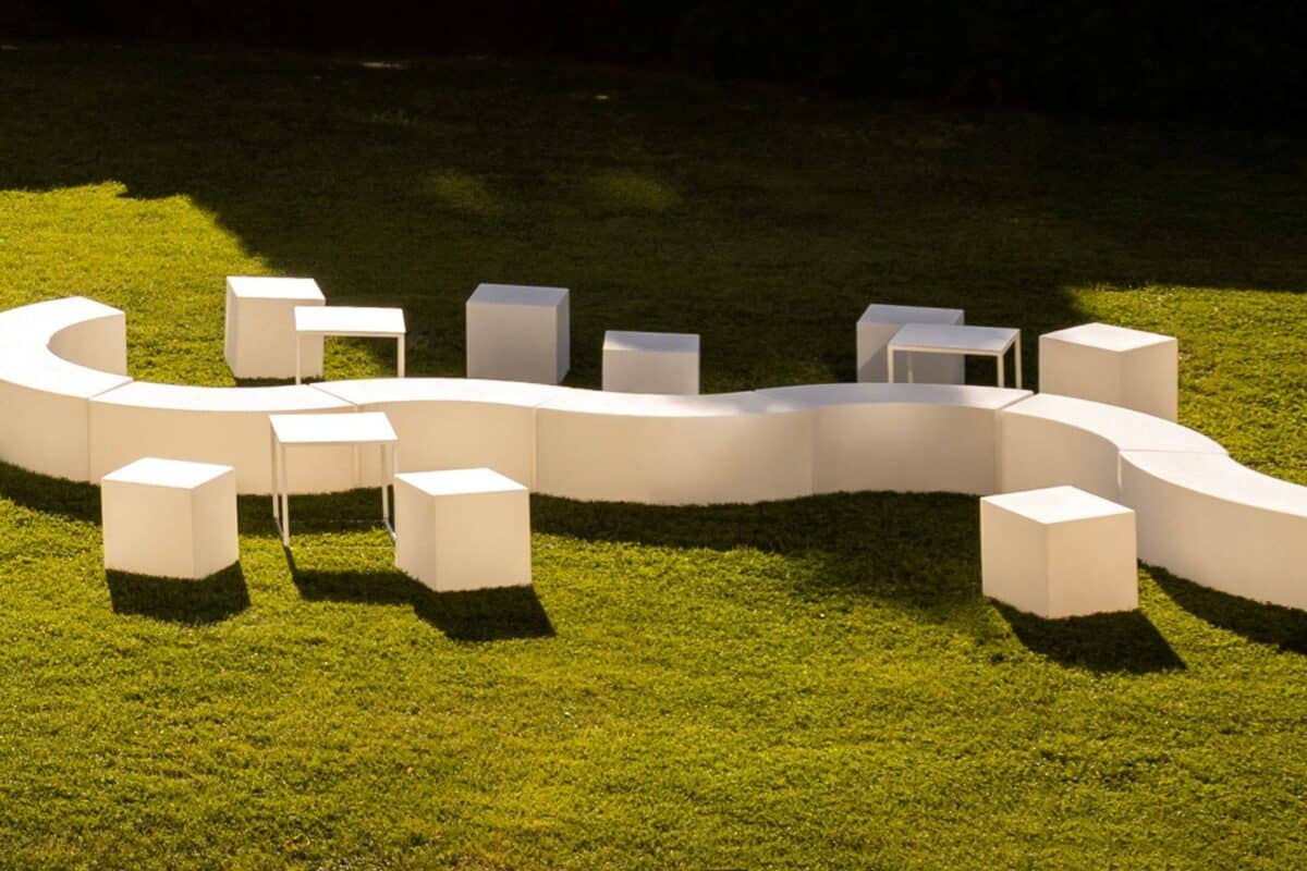 Seduta modulare bianca a forma di serpente con sgabelli abbinati su prato verde, ideale per eventi all'aperto e ambienti moderni.