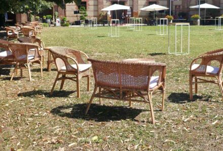 Sedie di vimini e tavoli all'aperto in un giardino soleggiato con ombrelloni bianchi e strutture di gioco.