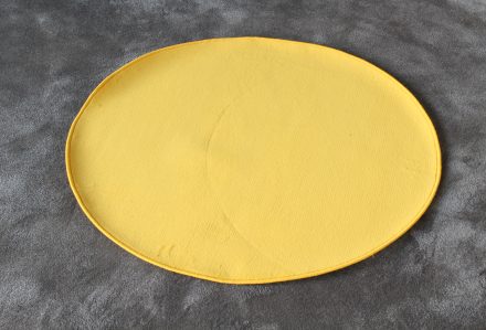 Un "Tappeto rotondo diam. 100 cm" di colore rosso è appoggiato su una superficie grigia testurizzata.