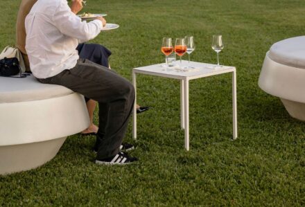 Persona che si rilassa all'aperto con un bicchiere di vino e cibo, seduta su un divano rotondo bianco su prato verde.
