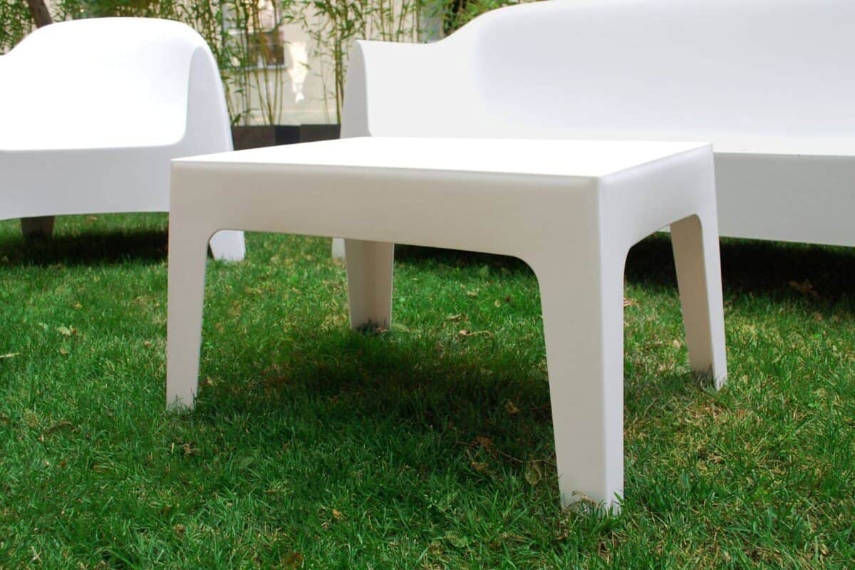 Tavolino bianco moderno in plastica su prato verde, arredamento esterno elegante e minimalista.