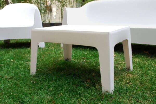 Tavolino bianco moderno in plastica su prato verde, arredamento esterno elegante e minimalista.