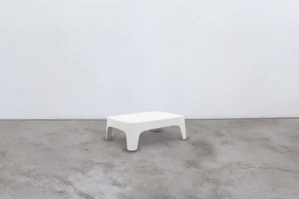 A white stool sitting on a concrete floor.