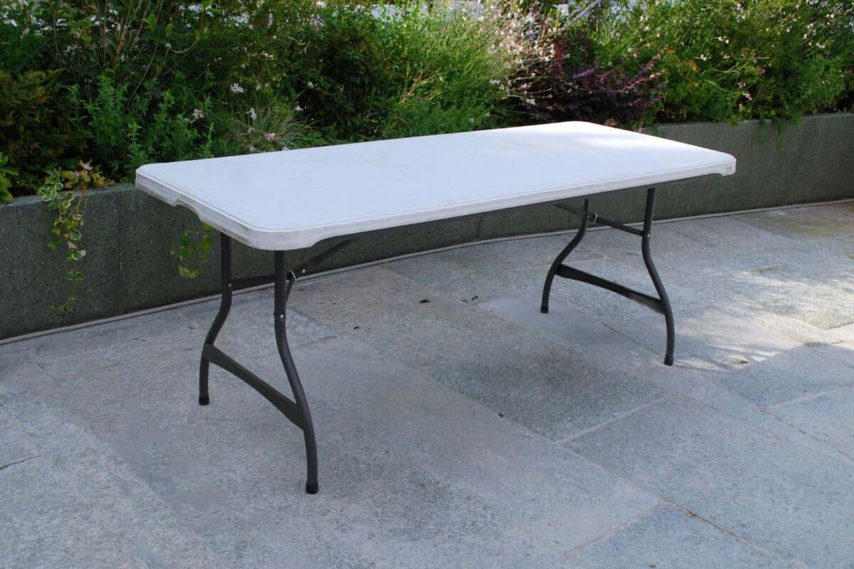 Tavolo da esterno pieghevole con piano in plastica bianca e struttura in metallo nero, ideale per giardini e terrazzi.