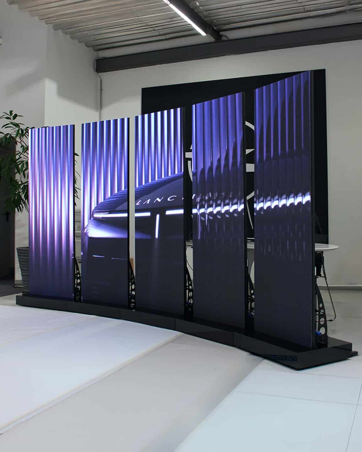 Display di schermi LED verticali con immagine di un'auto futuristica in un ambiente moderno.