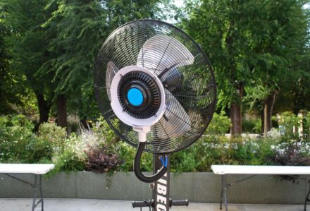 Ventilatore da esterno con grande girante in un parco verde, ideale per rinfrescare durante le giornate calde.