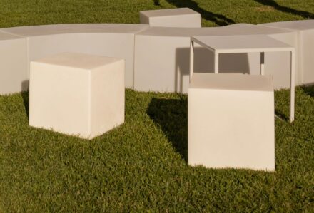 Set di arredi da esterno minimalisti con tavolo e sedie bianche su prato verde.