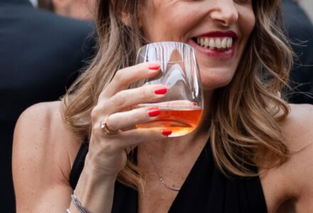 Bicchiere modello Tumbler acqua Invino da 37 cl a forma di calice senza stelo, tenuto in mano da una donna durante un brindisi, disponibile a noleggio con Modorent.